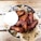 A metal bowl filled with crispy, golden-brown chicken wings arranged on a bed of brown paper with a decorative pattern. A small cup of creamy white sauce accompanies the wings, placed to the side. The setup is on a wooden table, enhancing the rustic and appetizing presentation.