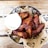 A metal bowl filled with crispy, golden-brown chicken wings arranged on a bed of brown paper with a decorative pattern. A small cup of creamy white sauce accompanies the wings, placed to the side. The setup is on a wooden table, enhancing the rustic and appetizing presentation.