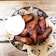 A metal bowl filled with crispy, golden-brown chicken wings arranged on a bed of brown paper with a decorative pattern. A small cup of creamy white sauce accompanies the wings, placed to the side. The setup is on a wooden table, enhancing the rustic and appetizing presentation.