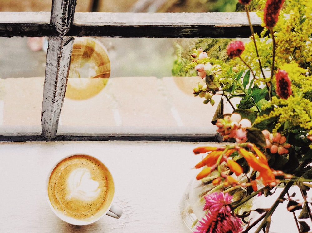 a cup of coffee sitting next to a vase of flowers