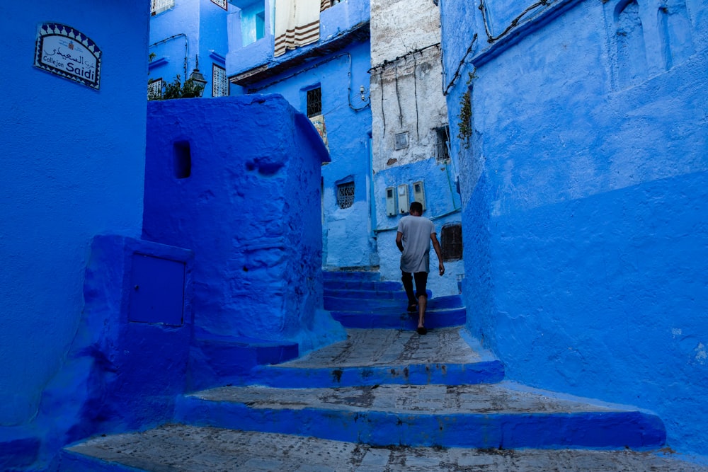 man walking up staircase between blue concrete buildings