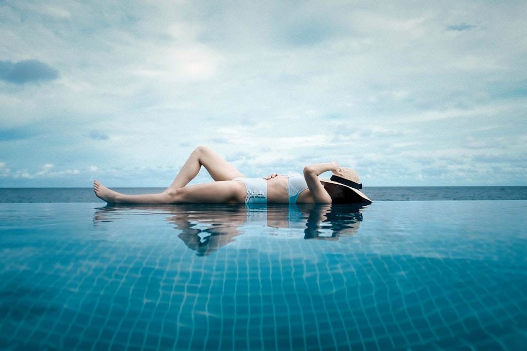 woman lying at the side of the pool during day,