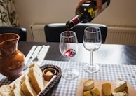 A glass of red wine being poured next to a plate with artisan cheese slices.