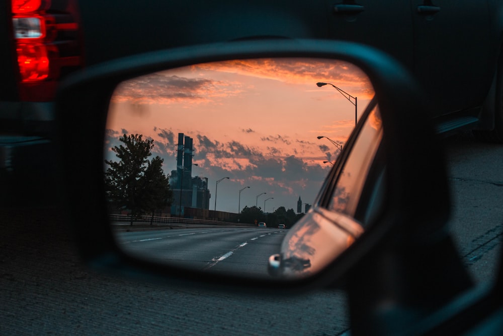 car side mirror view of road and lampposts during golden hour