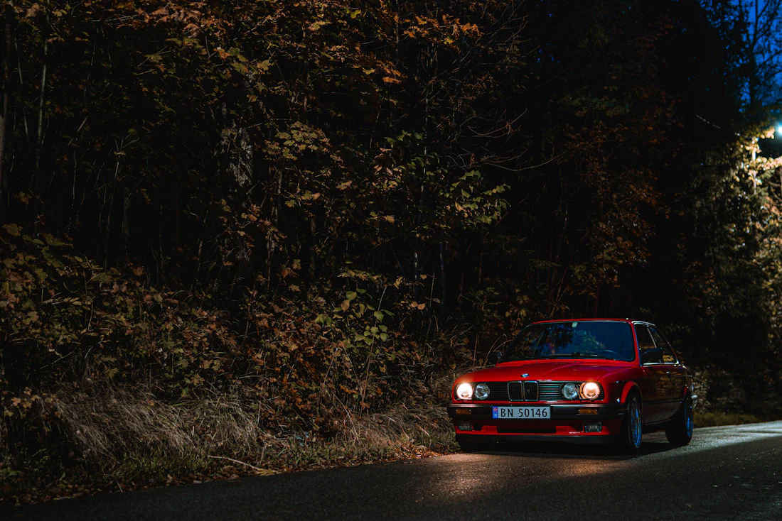 Deep red classic GT car on a shaded forest road at dusk