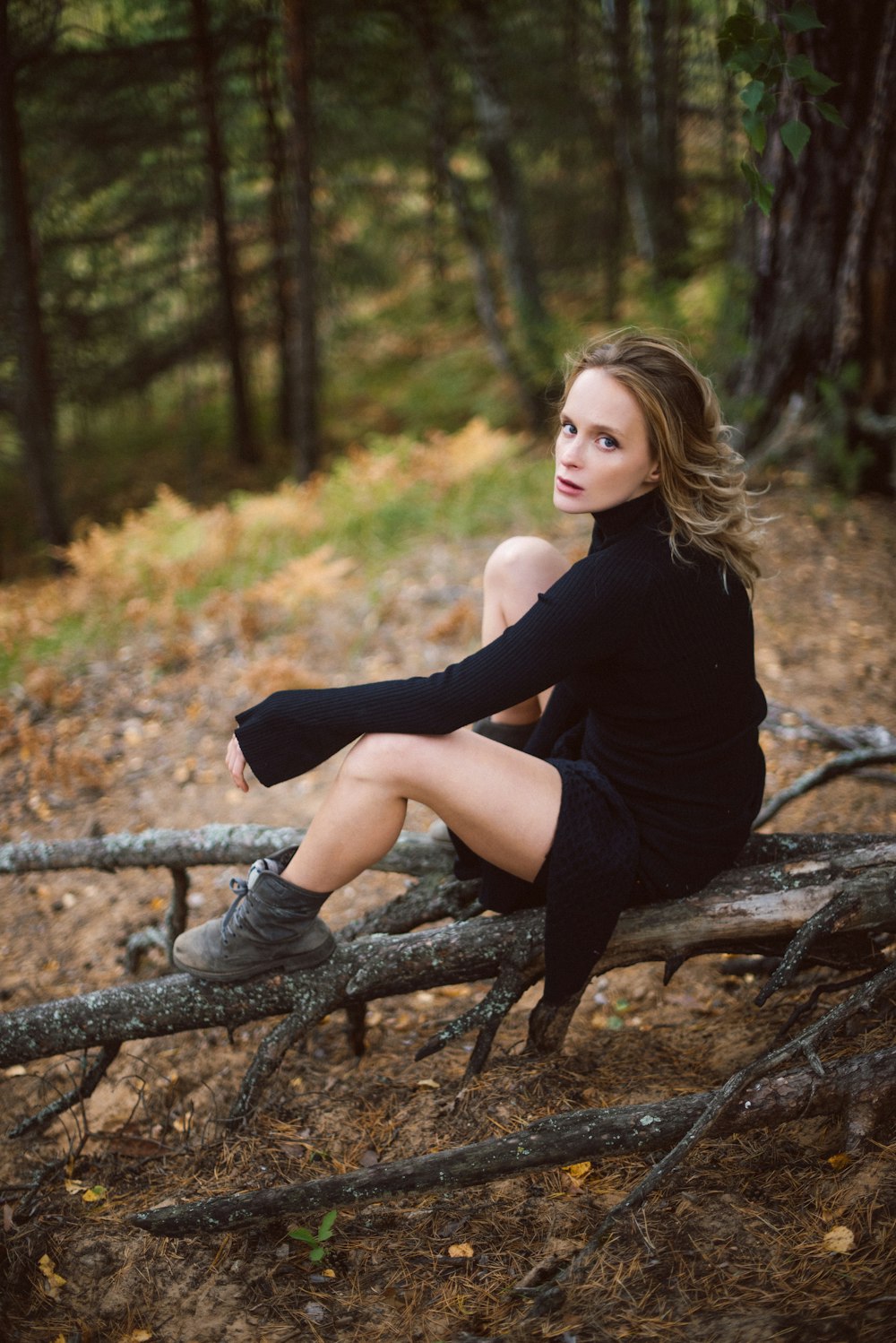 woman wearing black turtleneck sweater sitting on log while glancing her left side