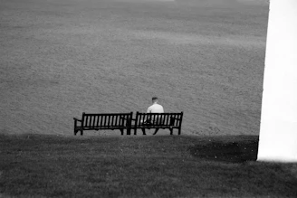 man sitting on bench facing the body of water during day