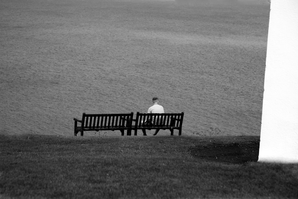 man sitting on bench facing the body of water during day