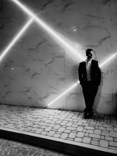 A man dressed in a sharp, modern suit from the men's collection, leaning casually against a marble wall.