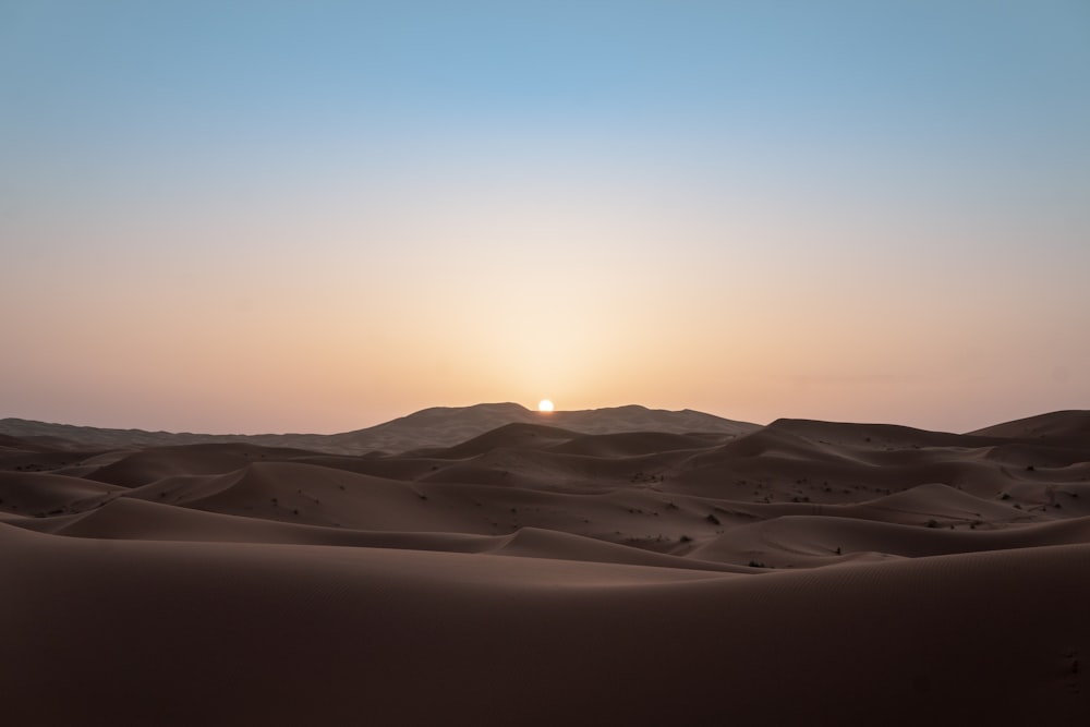 the sun is setting over the sand dunes