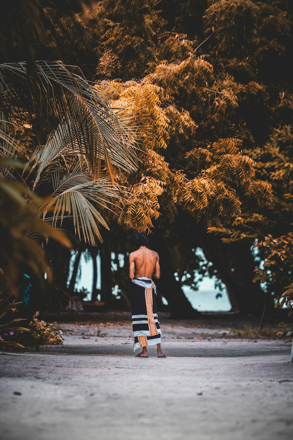 topless man with scarf wrapped around his body stands near trees