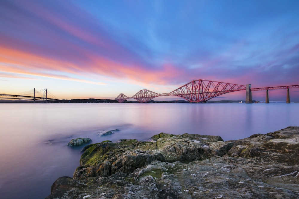 view of red suspension bridge under pink and blue sky