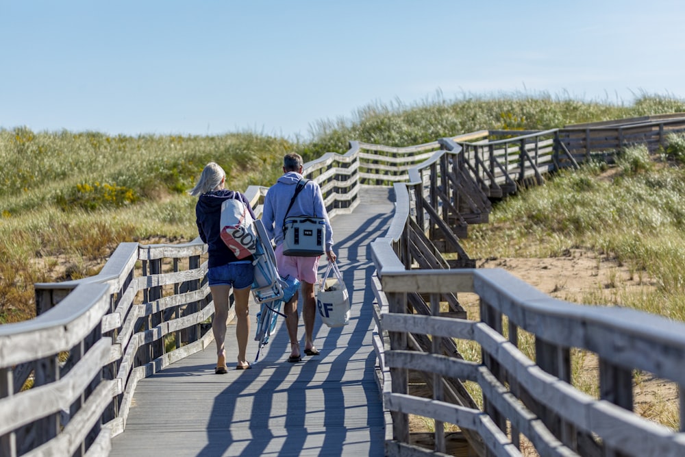 man and woman walking on wooden bridge besides grassland