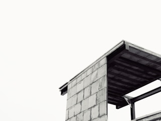 A modern, minimalistic structure with exposed beams and concrete surfaces stands against a plain, overcast sky. The angular lines and the simplicity of design give a sense of starkness and functionality.