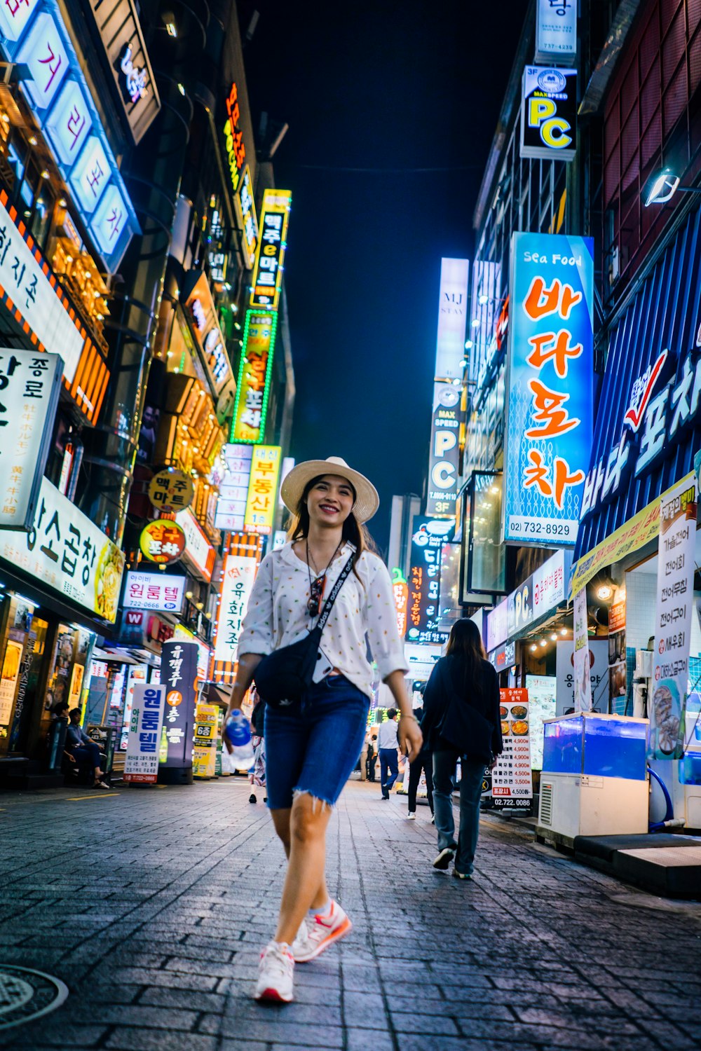 femme marchant entre des bâtiments avec des panneaux lumineux la nuit