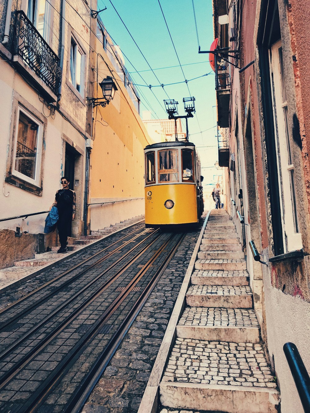 people walking near tram in between buildings during daytime