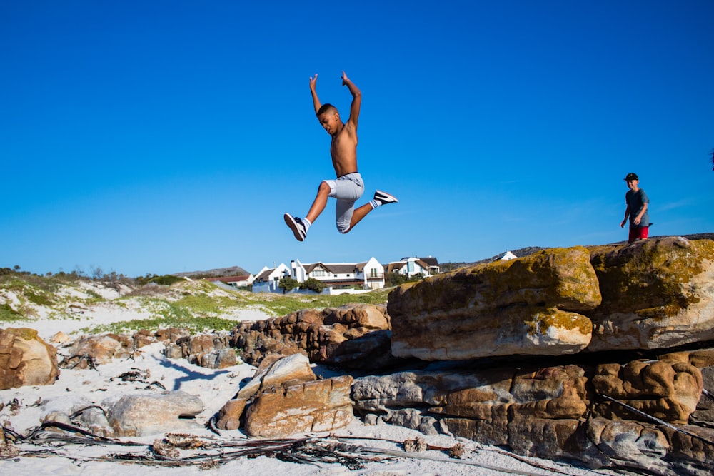 topless boy jumping from cliff under blue and white sky during daytime