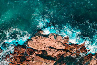 A dramatic shot of crashing ocean waves along a rugged coastline taken from above.