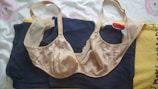 A beige lace bra is laid over a navy blue garment and a piece of yellow fabric. The background is white with subtle pink and green floral patterns.