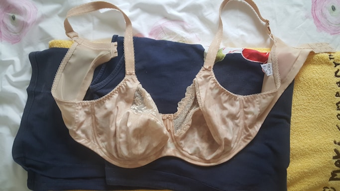 A beige lace bra is laid over a navy blue garment and a piece of yellow fabric. The background is white with subtle pink and green floral patterns.