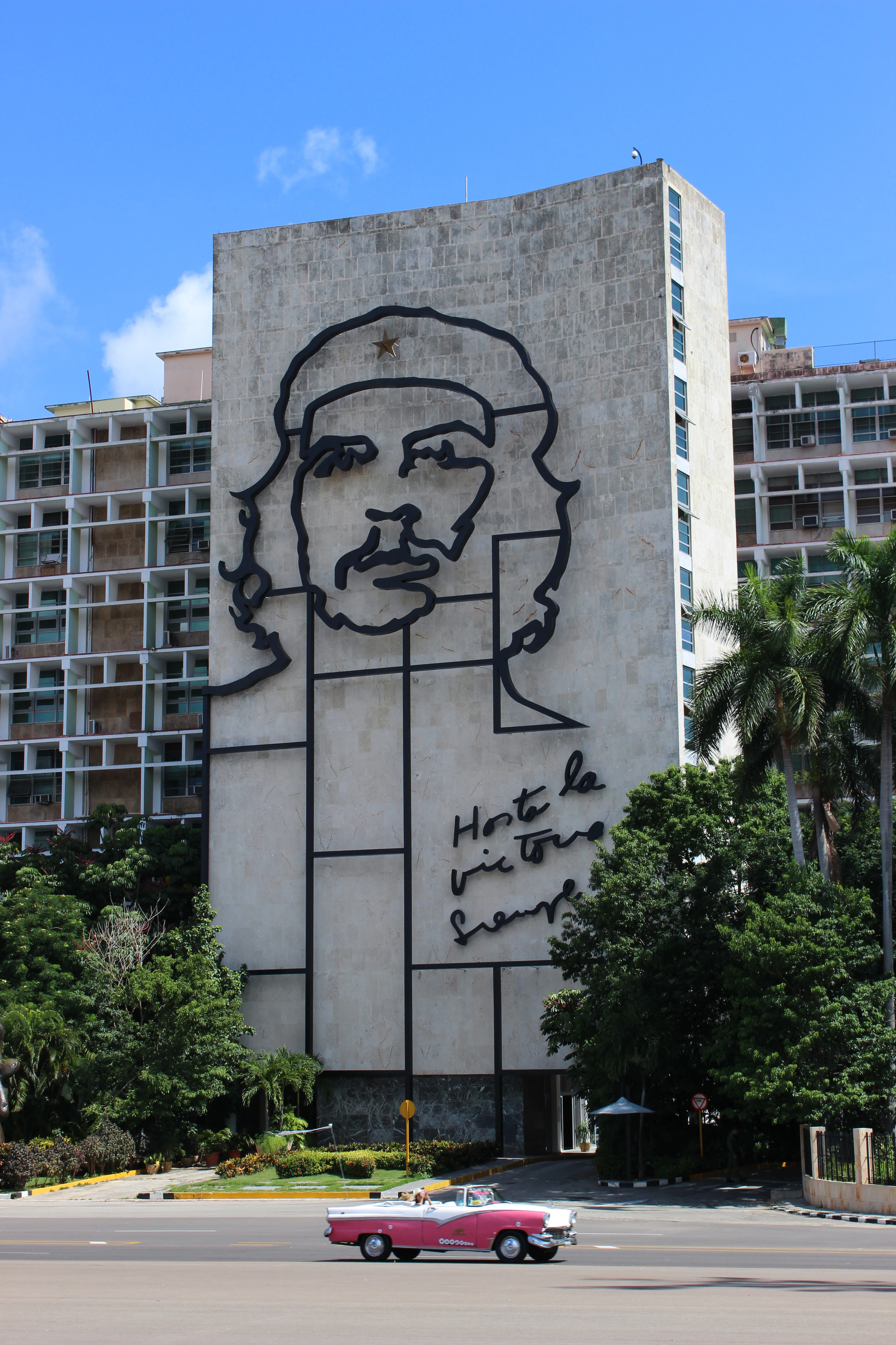 The steel Che Guevara mural on the Ministry of the Interior at Plaza de la Revolucion, a pink vintage car passing below