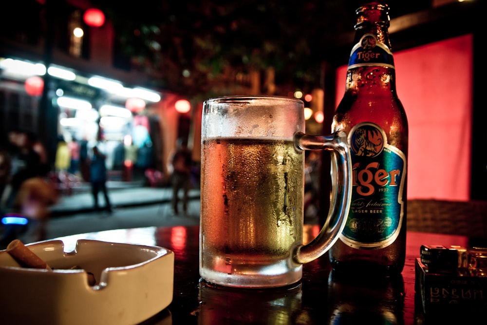 beer mug on top of table near ashtray and Tiger beer bottle