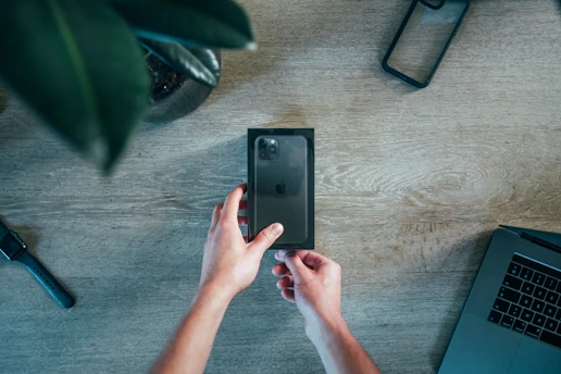 Close-up of hands testing a new smartphone with tech accessories on a desk.
