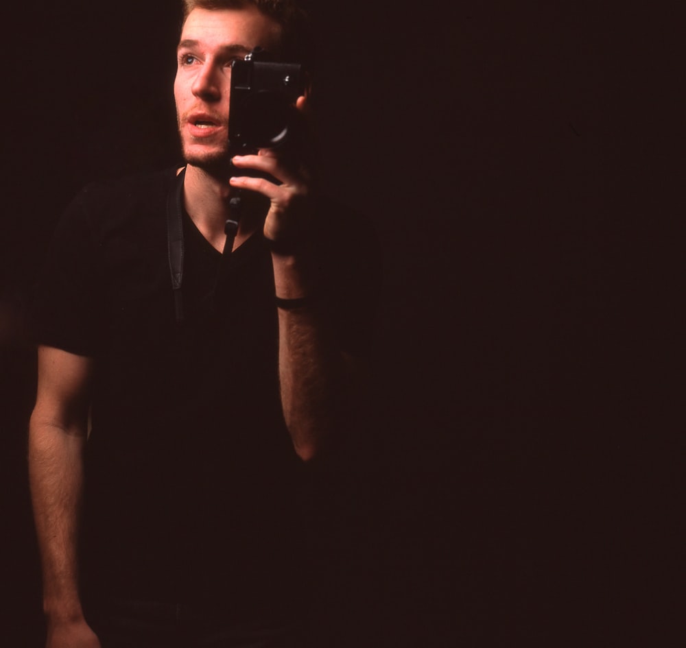 homme portant un t-shirt noir à col en v tenant un smartphone