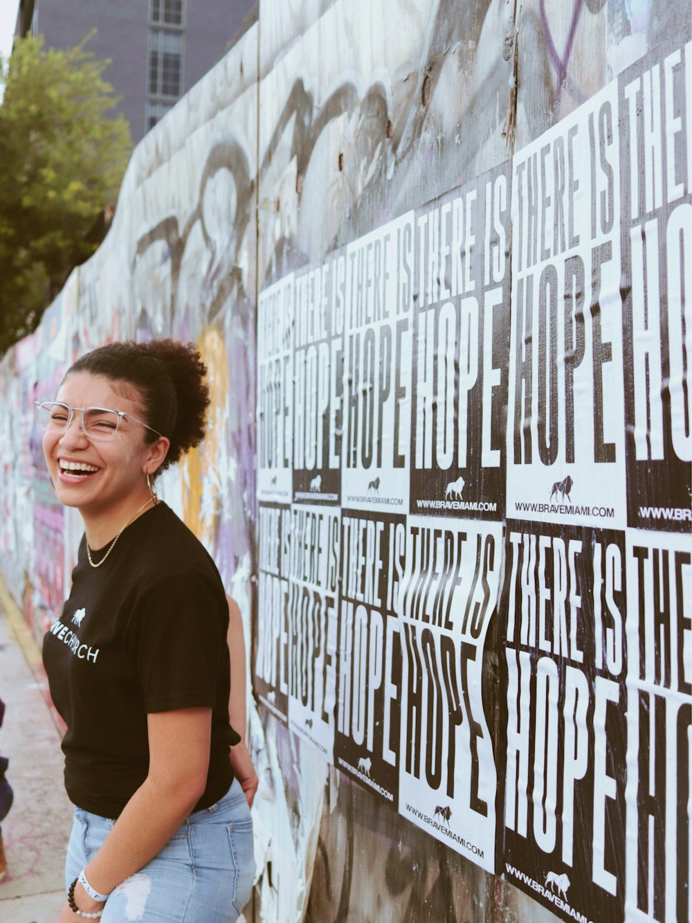 woman stands on the sidewalk behind There is Hope posters on the wall