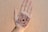 A hand is displayed with intricate henna artwork applied to the palm. The design is symmetrical and features floral and circular motifs in a dark brown color. The hand is positioned against a textured, circular backdrop.