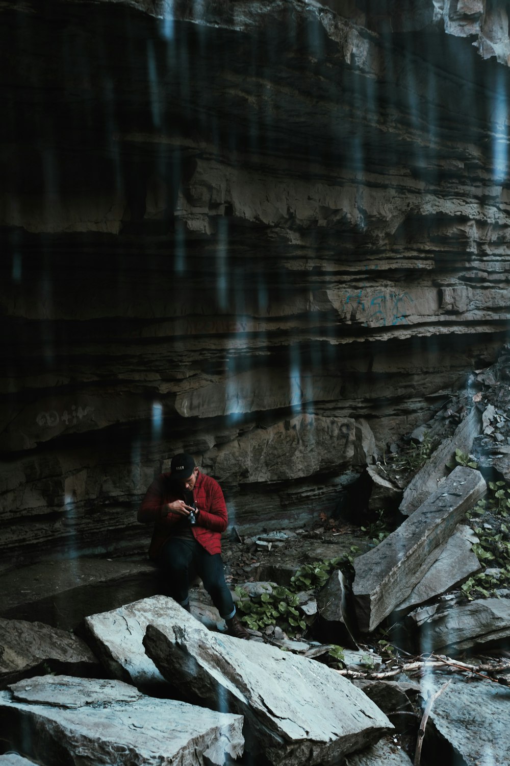 man wearing red jacket standing beside rocks