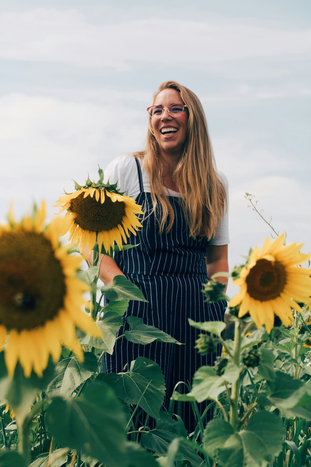 woman wearing white and blue pinstriped jumpsuit surrounded by sunflowers