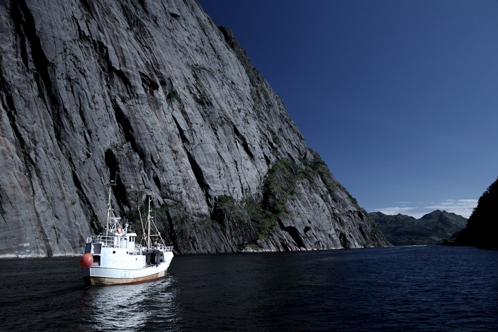 white boat on body of water beside gray cliff