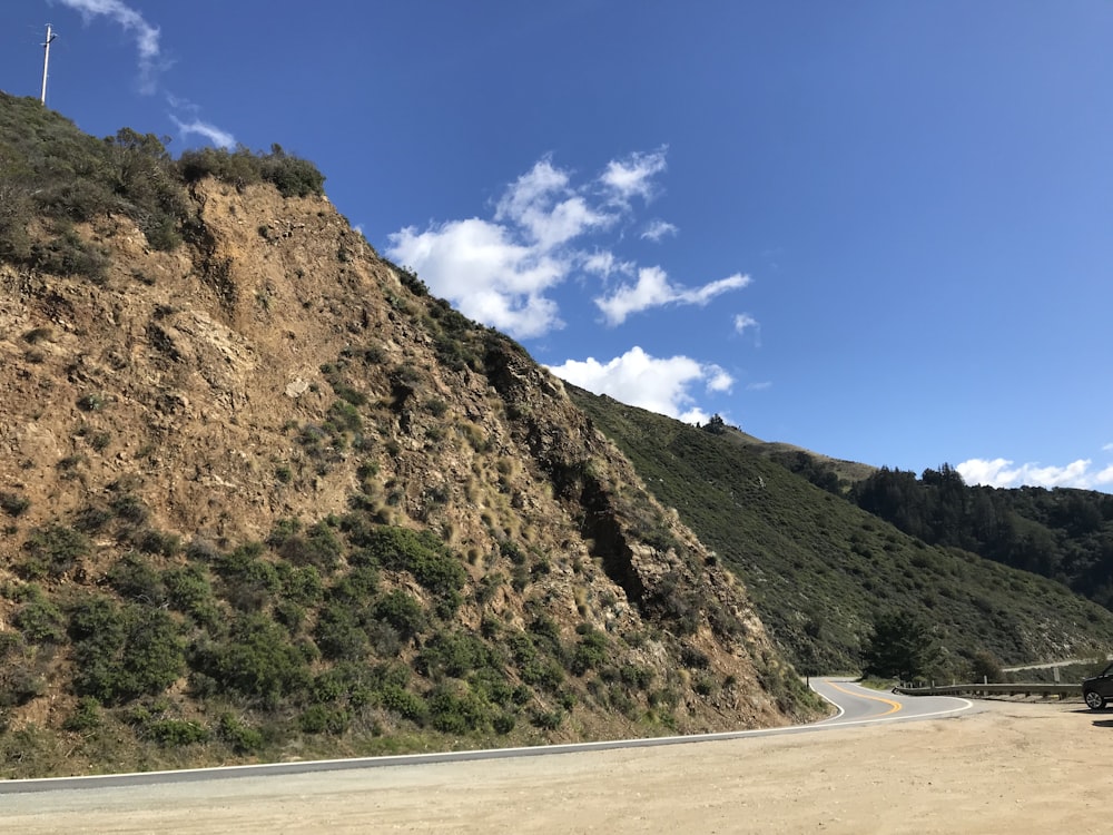 asphalt road beside mountain under blue sky