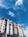 A multi-story residential building featuring a mix of red, beige, and white colors along with large white columns. The sky in the background is bright and blue with scattered white clouds. Some utility wires are visible in the foreground.