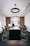 A modern office with a long wooden conference table surrounded by black chairs. The back wall features wooden slats and shelves displaying trophies and decorative items. A circular ceiling light hangs above the table, and natural light enters from windows on the side.