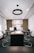 A modern office with a long wooden conference table surrounded by black chairs. The back wall features wooden slats and shelves displaying trophies and decorative items. A circular ceiling light hangs above the table, and natural light enters from windows on the side.