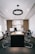A modern office with a long wooden conference table surrounded by black chairs. The back wall features wooden slats and shelves displaying trophies and decorative items. A circular ceiling light hangs above the table, and natural light enters from windows on the side.