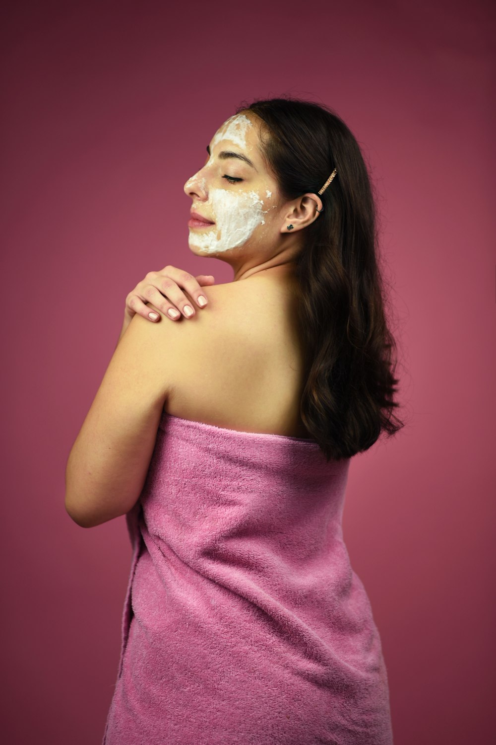woman looking over her left shoulder wearing pink towel and white cream mask