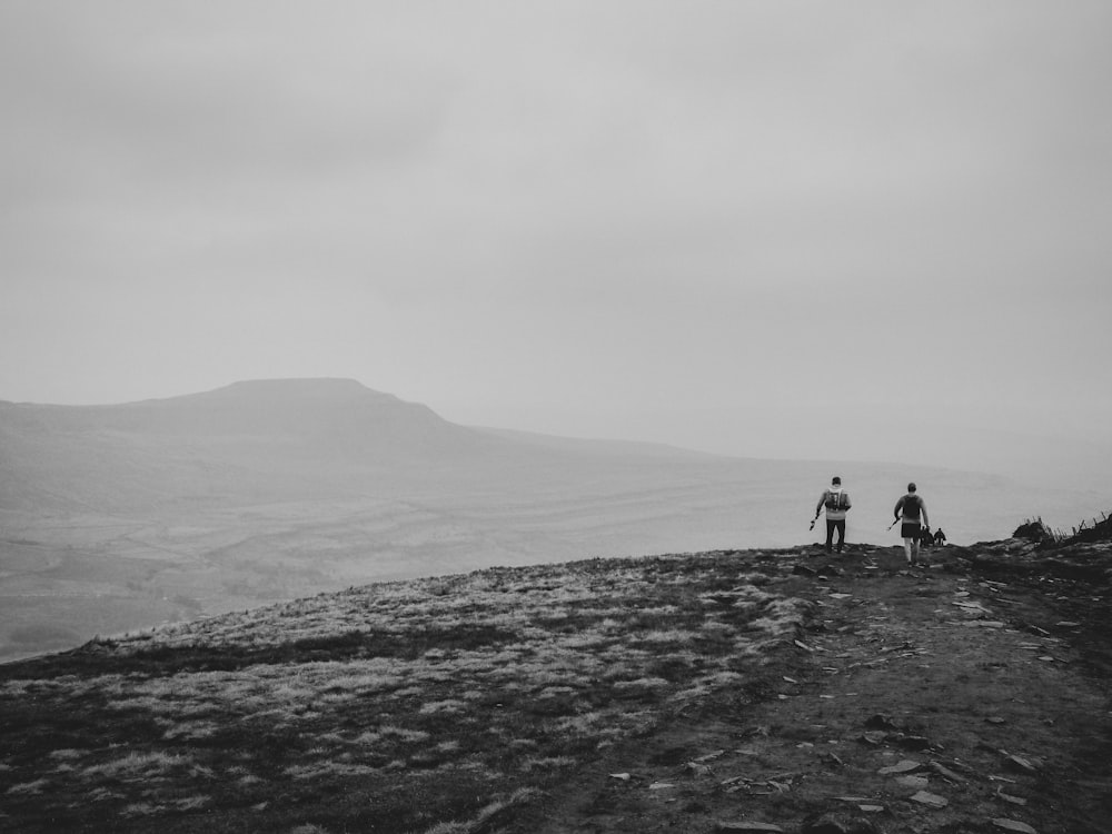 grayscale photography of two people on cliff