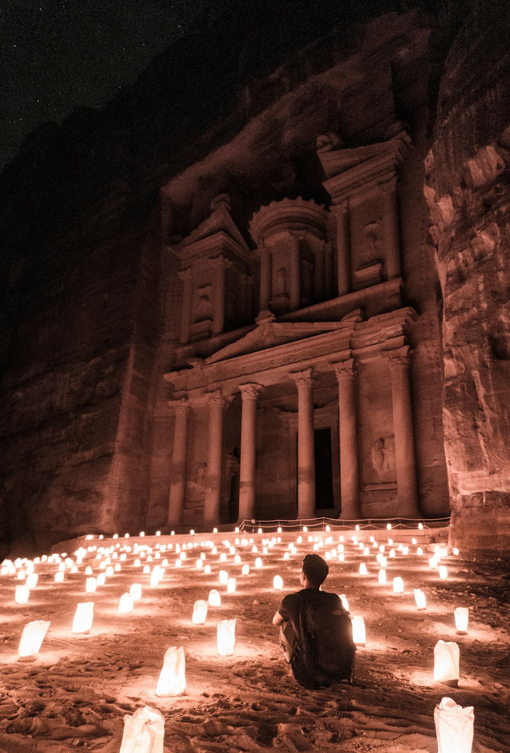 man sitting on ground surrounded by lantern lamp lot outside buildings