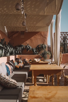 A cozy outdoor seating area with cushioned benches and a wooden table under a shaded garden structure.