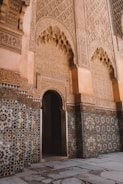 Intricate Islamic architecture featuring detailed geometric patterns and decorative Arabic calligraphy on the walls. The design includes large archways and a combination of mosaic tiles with floral and traditional motifs.