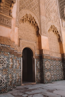 Intricate Islamic architecture featuring detailed geometric patterns and decorative Arabic calligraphy on the walls. The design includes large archways and a combination of mosaic tiles with floral and traditional motifs.