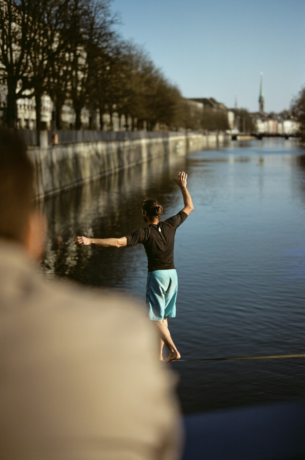 man wearing black shirt walking on rope near body of water