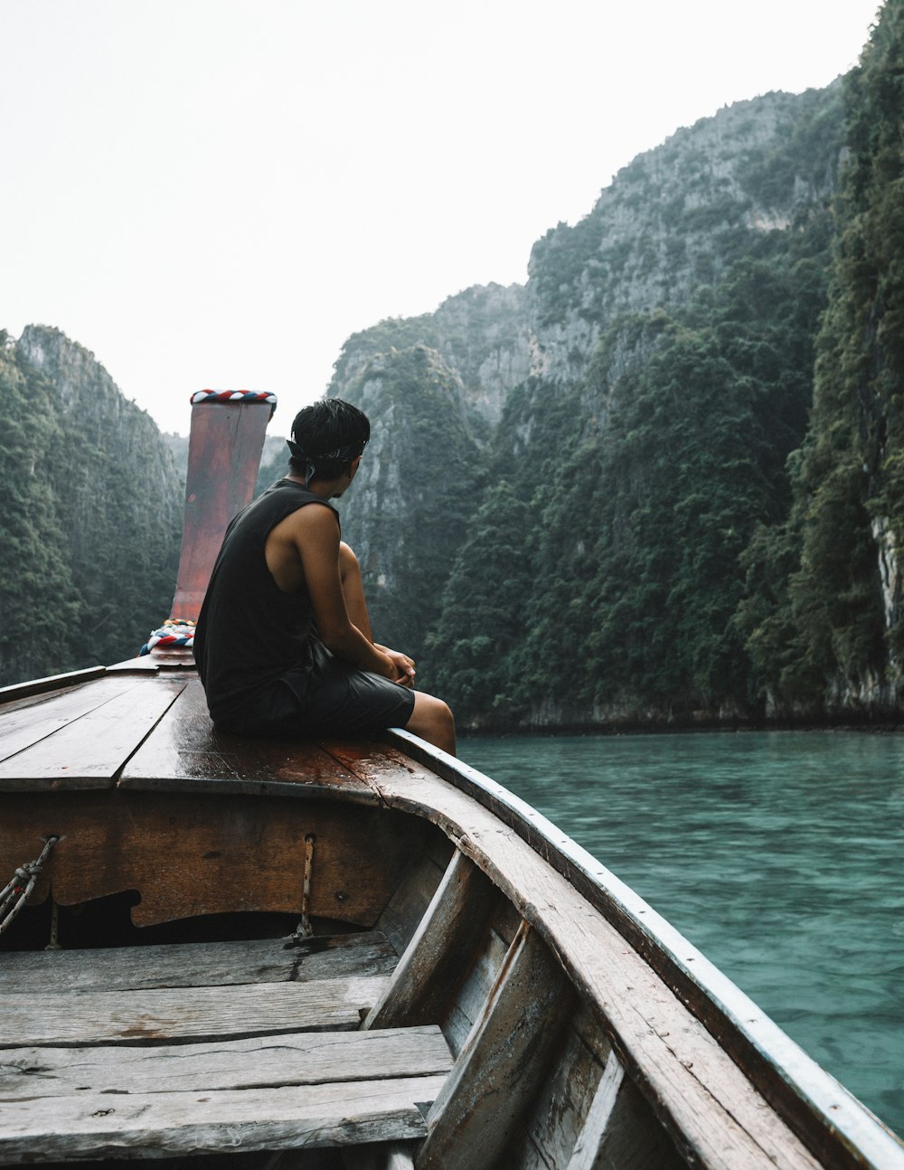 man sitting on brown wooden boat in body of water during daytime