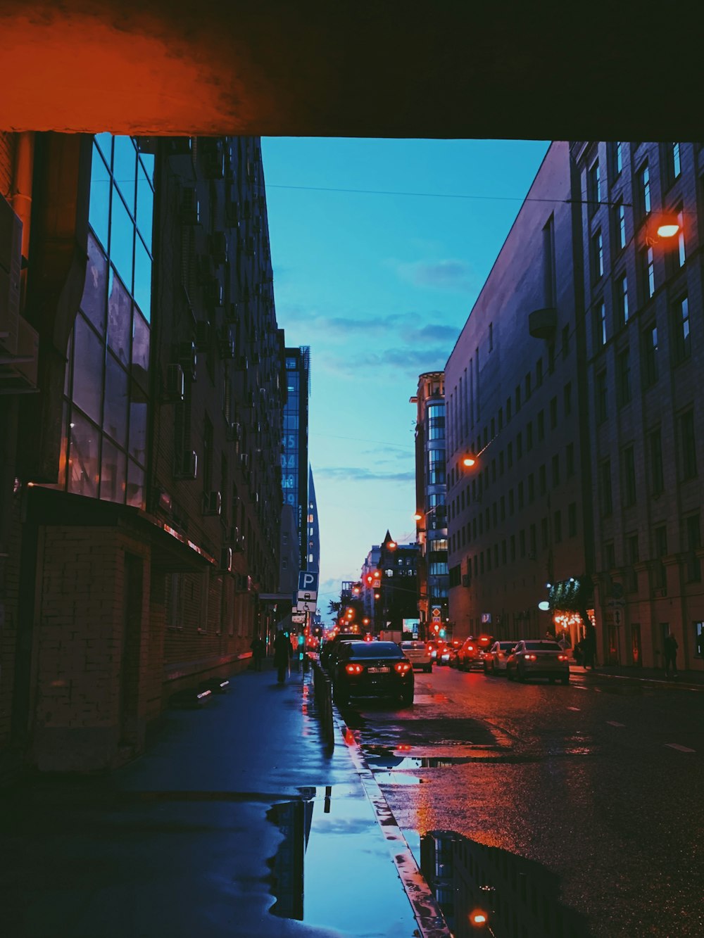 people walking on pathway near buildings and different vehicles on road during night time