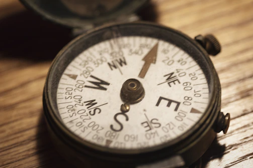 A close-up of a map with marked routes and a compass on a wooden table.