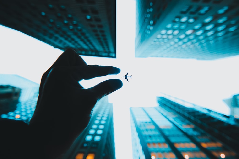 person's left hand on air near buildings under plane in low-angle view photography