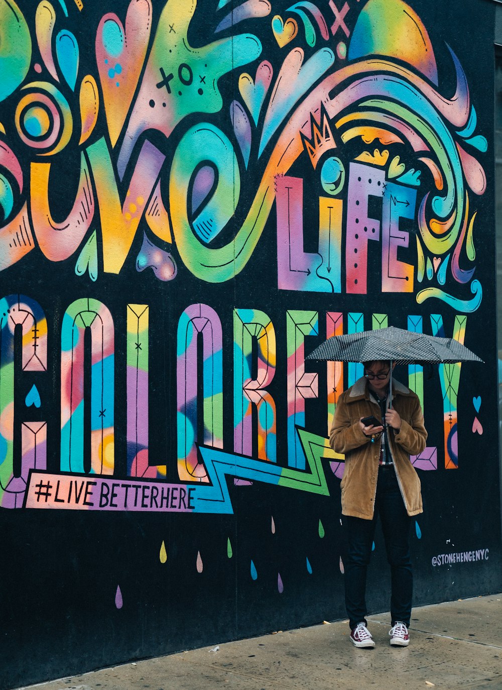 person holding umbrella while using smartphone near graffiti wall